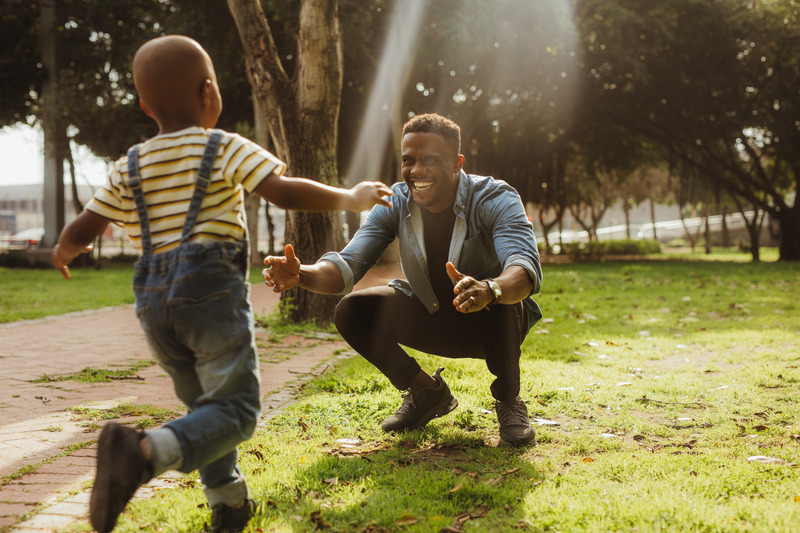 Man crouching at the park with his arms outstretched, with a boy running towards him. Son running into father's arms.
