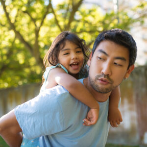 Hombre asiático y niña divirtiéndose en el parque de verano. Padre alegre sosteniendo a su hija sonriente en su espalda caminando en el parque pasando el fin de semana juntos. Infancia, ocio, concepto de descanso de verano